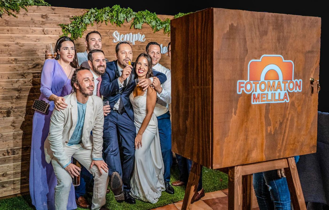 Novios e invitados posando junto al fotomatón de madera en una boda